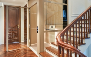 Elegant elevator with glass doors and wooden staircase in upscale building.