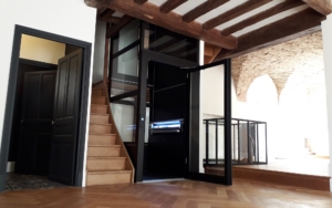 Contemporary home elevator with glass doors and wooden staircase.