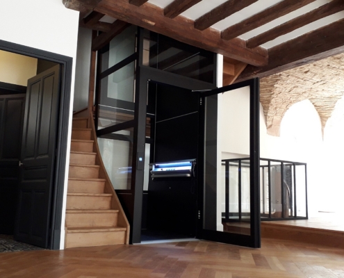 Contemporary home elevator with glass doors and wooden staircase.