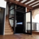 Contemporary home elevator with glass doors and wooden staircase.